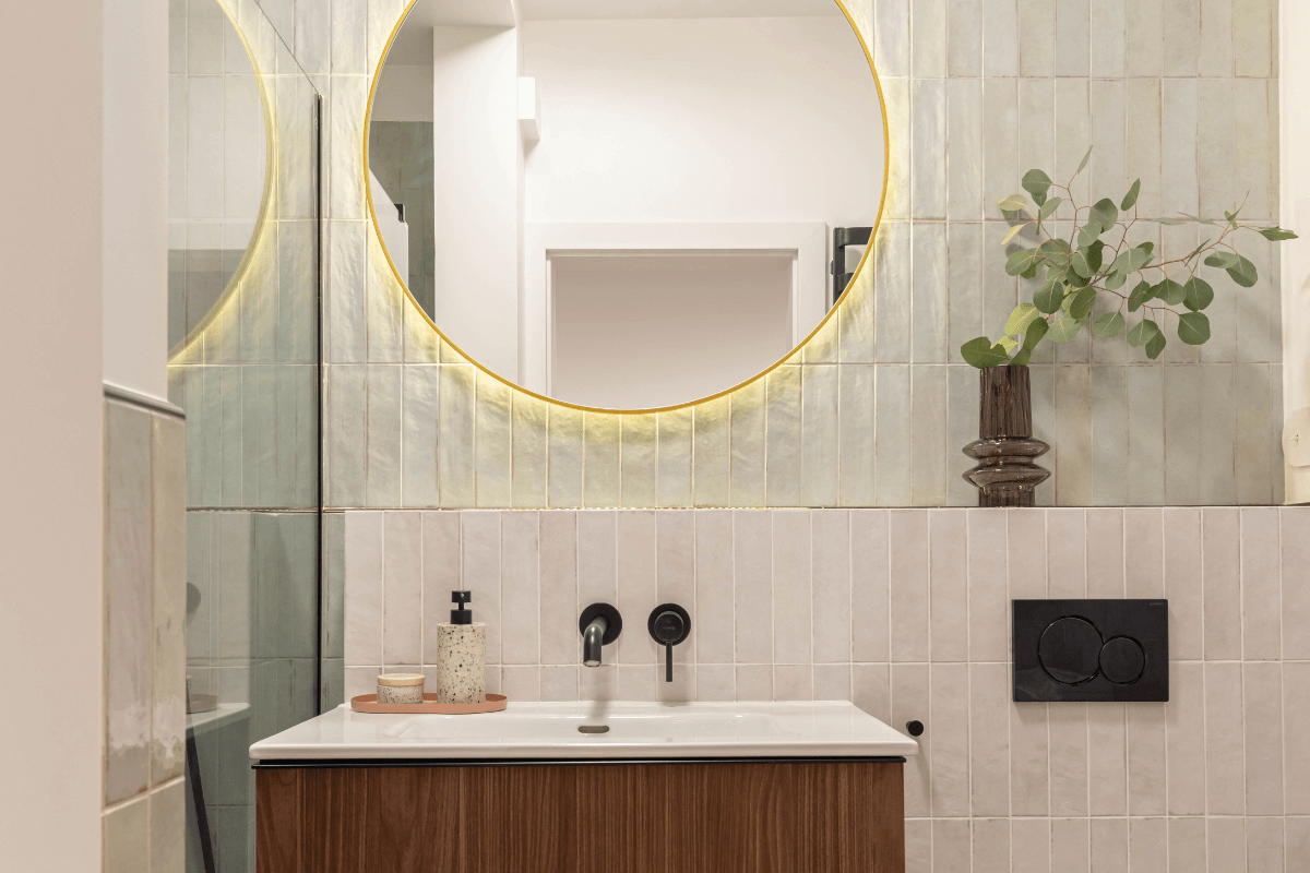 Nowoczesna łazienka z drewnianą szafką, okrągłym lustrem, płytkami w stylu art deco i eklektycznymi akcentami.