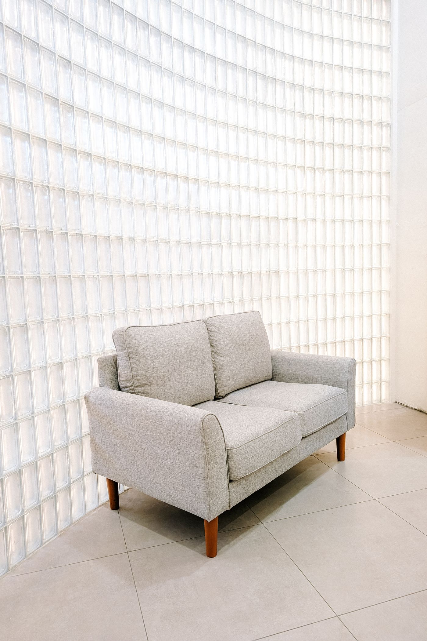 Jasna minimalistyczna sofa przy świecącej ścianie z luksferów