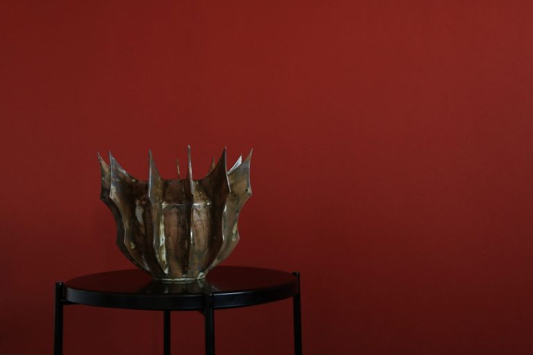 Ściana w głębokim kolorze bordo, przed nią czarny okrągły stolik z metalowym wazonem