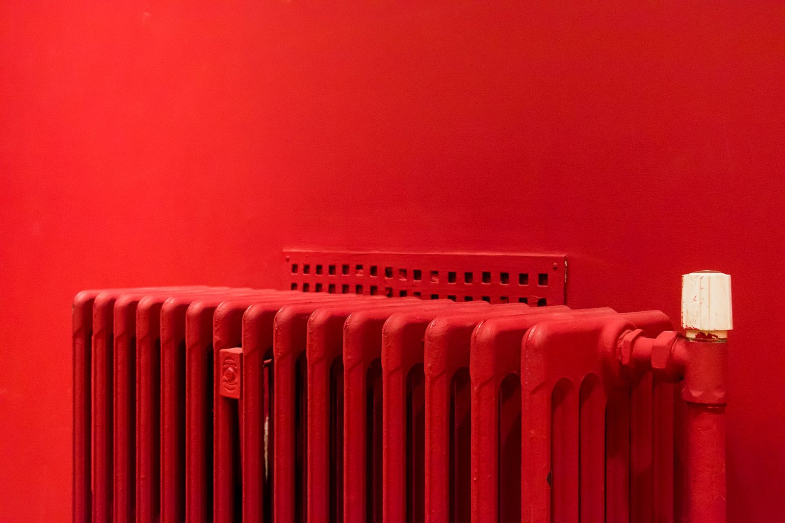 Czerwony żeliwny grzejnik kolumnowy na ścianie pomalowanej tym samym czerwonym kolorem