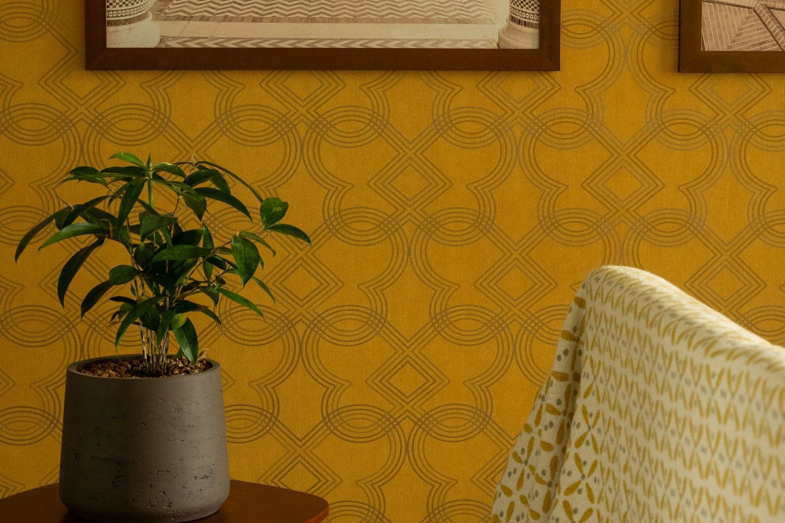 Żółta tapeta w geometryczny wzór w salonie, obok fotel i roślina w donicy