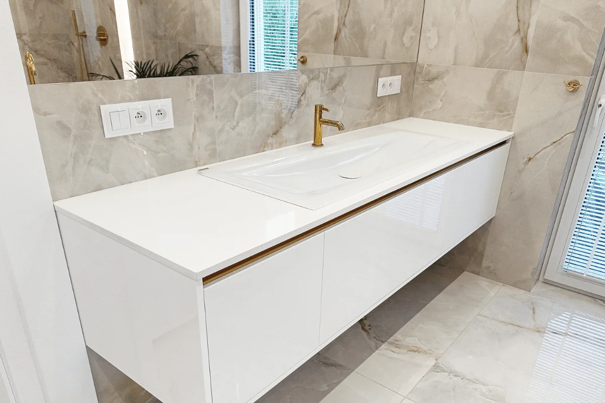 Nowoczesna łazienka z białą umywalką i złotymi detalami w stylu glamour.