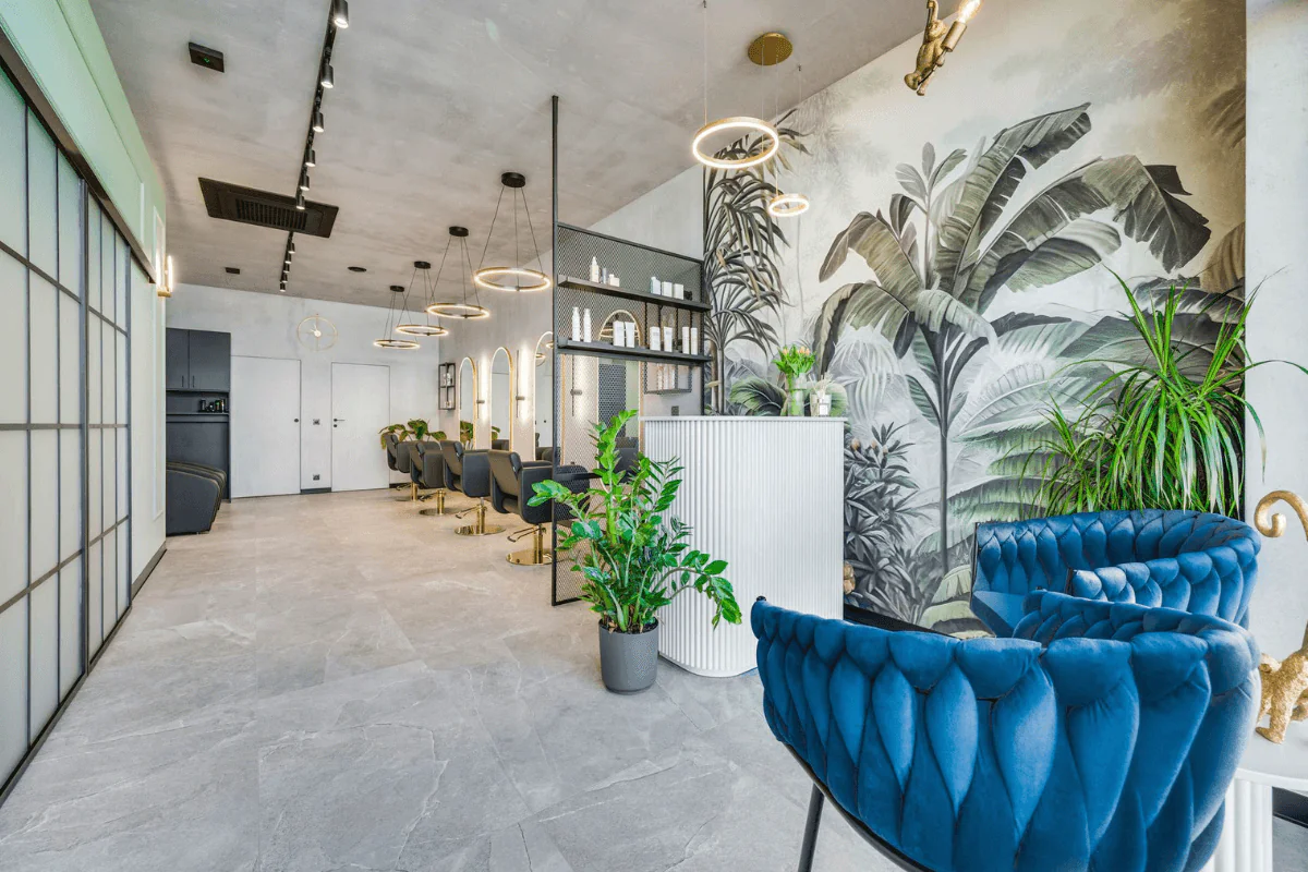 Wnętrze lokalu usługowego w stylu industrialnym i współczesnym z niebieskimi fotelami i roślinami.