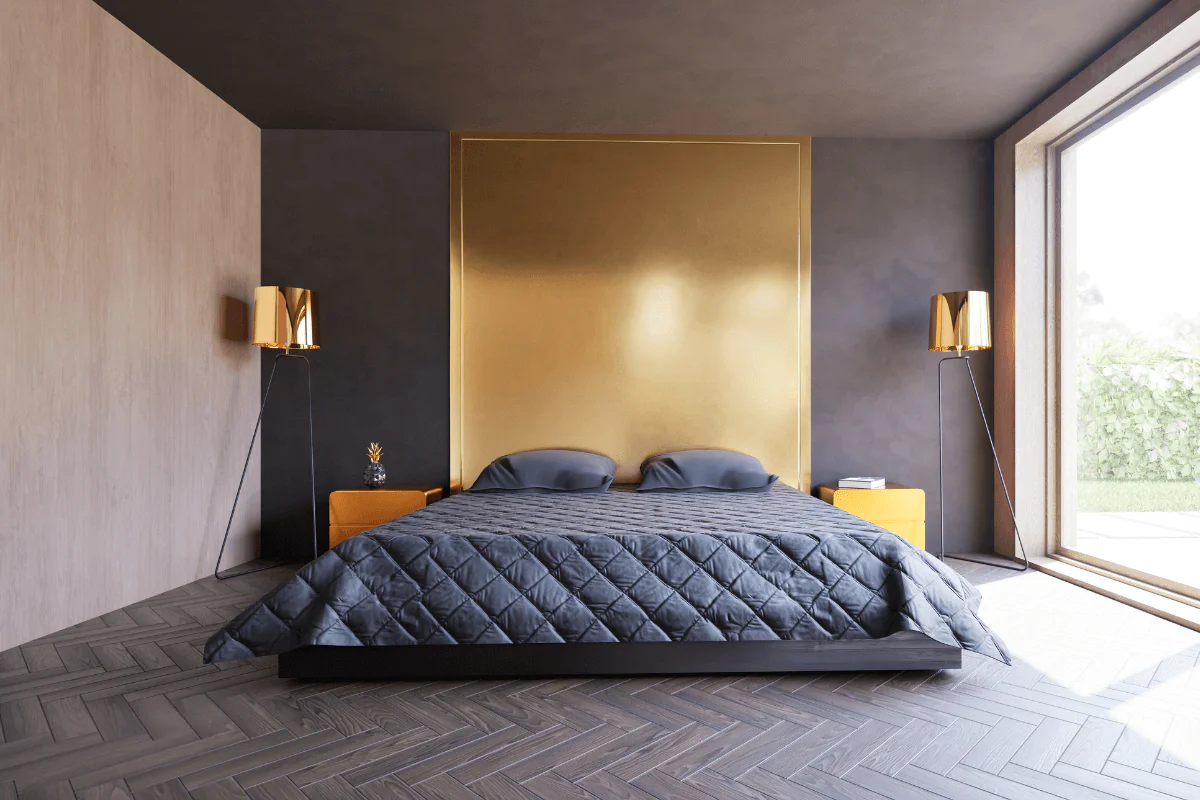 Sypialnia w nowoczesnym stylu z dużym, niskim łóżkiem, ciemnoszarą narzutą, złotym panelem dekoracyjnym na ścianie, designerskimi lampami i dużym oknem z widokiem na zieleń.