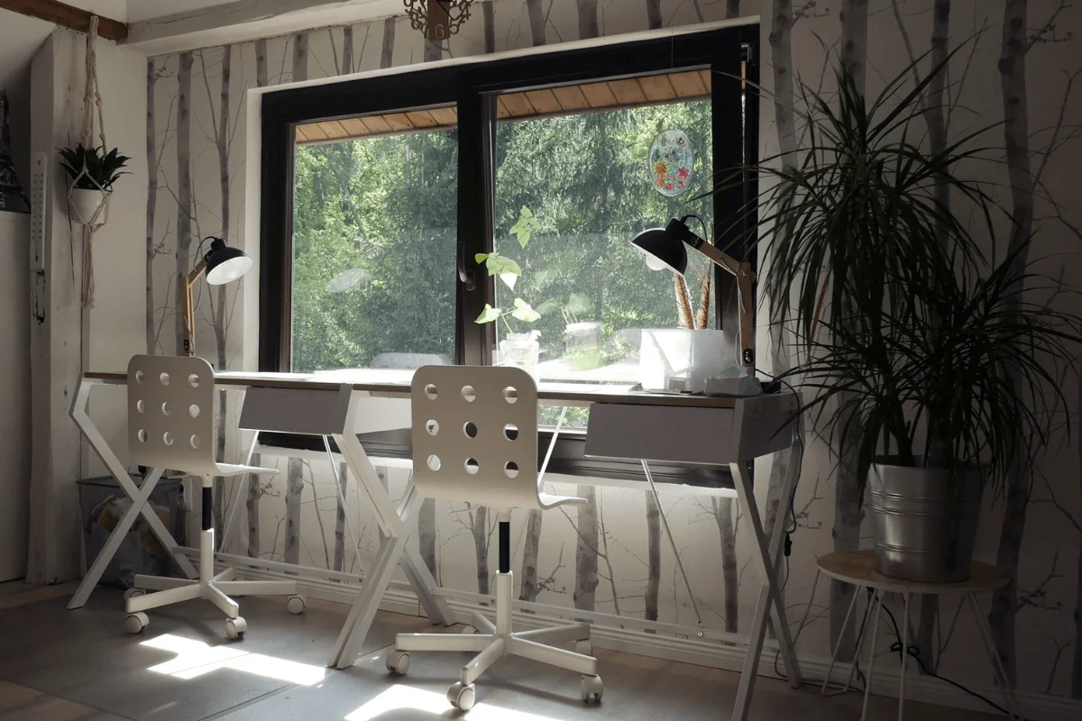 Wnętrze pokoju rodzeństwa ze skandynawskim designem, białe biurka, rośliny i duże okno.