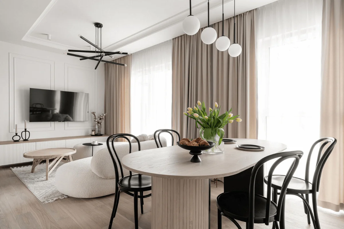 Wnętrze jadalni z jasnym stołem, czarnymi krzesłami i bukietem tulipanów.