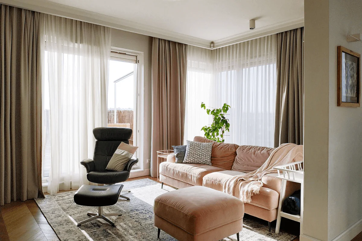 Wnętrze salonu z różową sofą, czarnym fotelem i rośliną w tradycyjnym stylu.