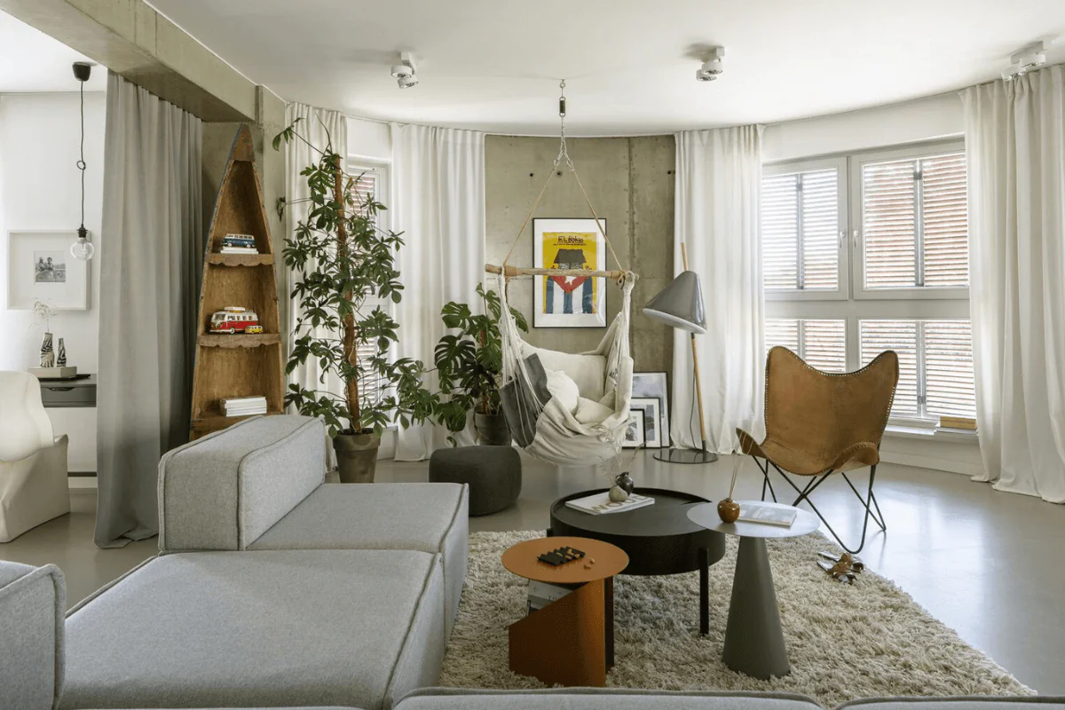Wnętrze salonu w stylu boho i industrialnym z szarym narożnikiem oraz roślinami.