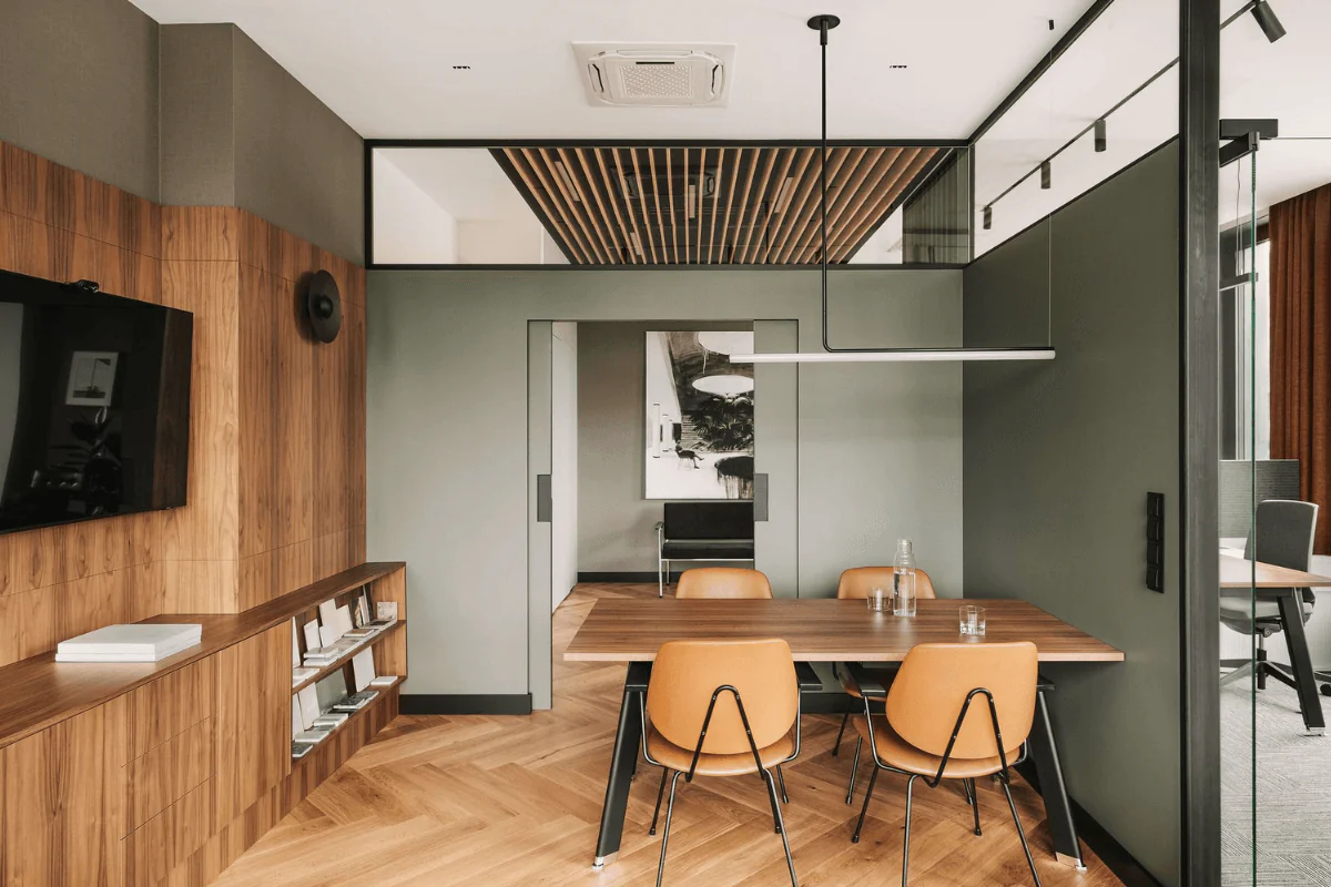 Wnętrze jadalni z drewnianym stołem, pomarańczowymi krzesłami i industrialnymi akcentami.