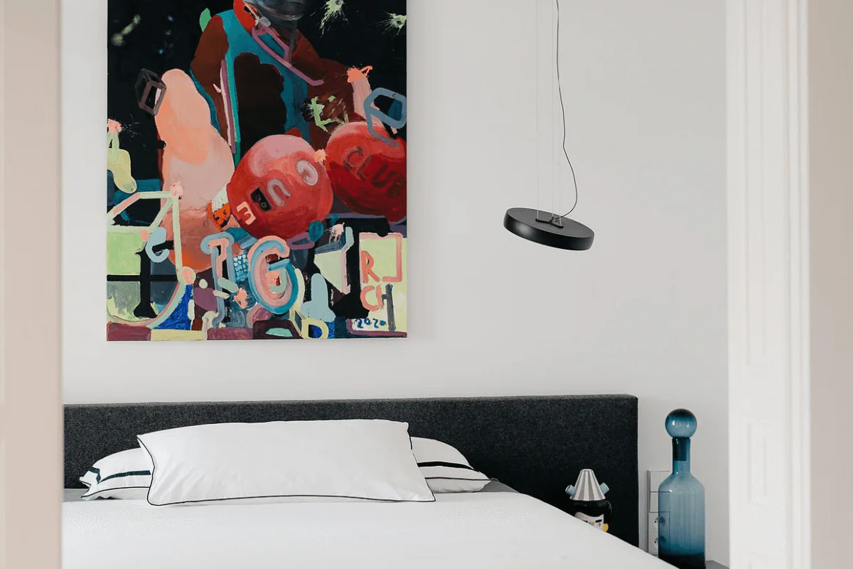 Sypialnia z minimalistycznym łóżkiem i eklektycznym obrazem na ścianie.