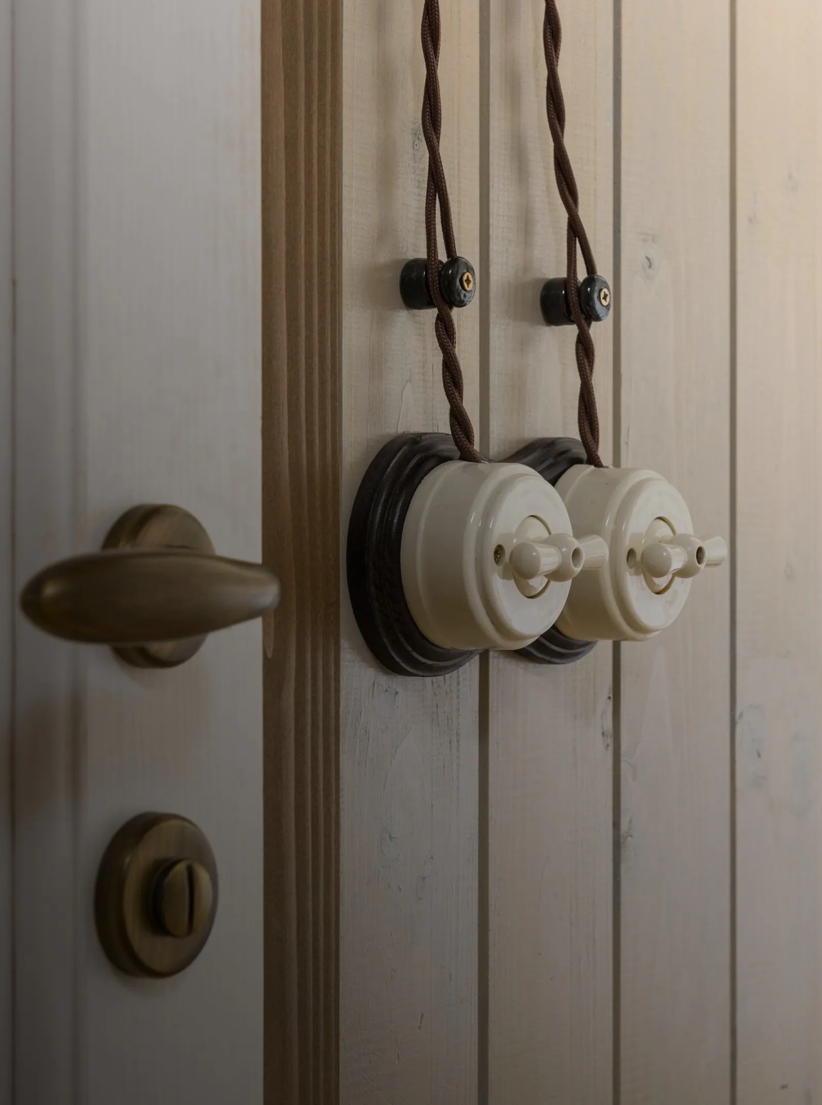 Ceramiczne włączniki retro w kremie z mosiężną klamką na jasnej boazerii