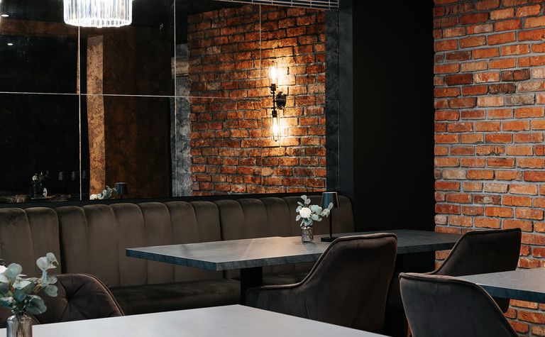 Wnętrze restauracji z ceglaną ścianą, eleganckimi meblami i industrialnym oświetleniem.