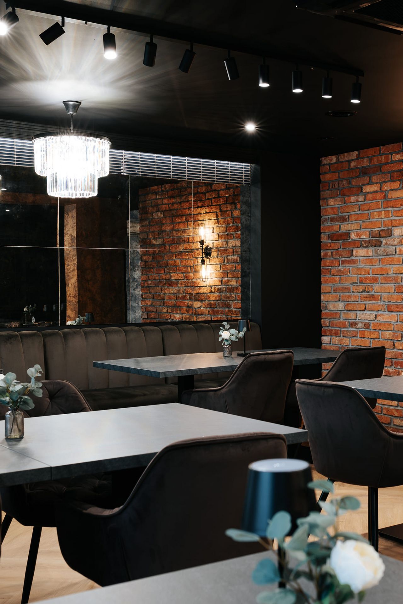 Wnętrze restauracji z ceglaną ścianą, eleganckimi meblami i industrialnym oświetleniem.