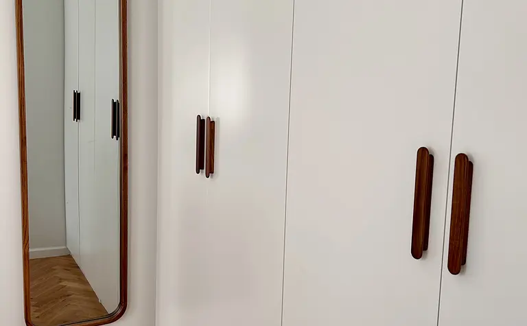 Garderoba w stylu eklektycznym i skandynawskim z białymi meblami i lustrem.