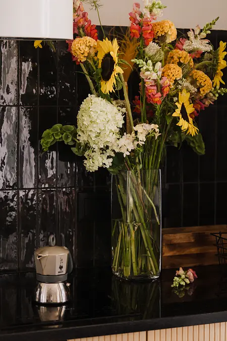 Współczesna kuchnia z czarnym blatem i wazonem z kwiatami.