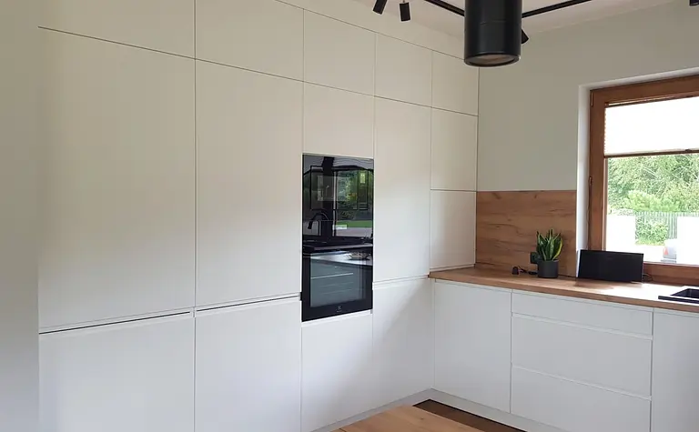 Nowoczesna kuchnia z białymi meblami i drewnianym akcentem w stylu industrialnym i skandynawskim.