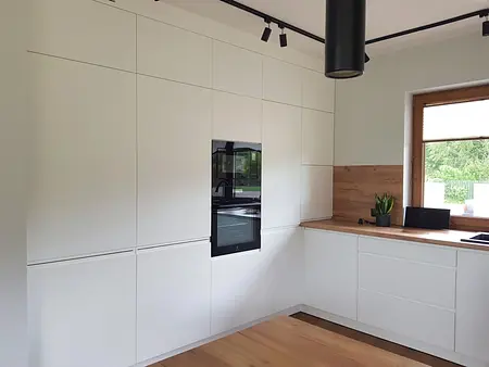 Nowoczesna kuchnia z białymi meblami i drewnianym akcentem w stylu industrialnym i skandynawskim.