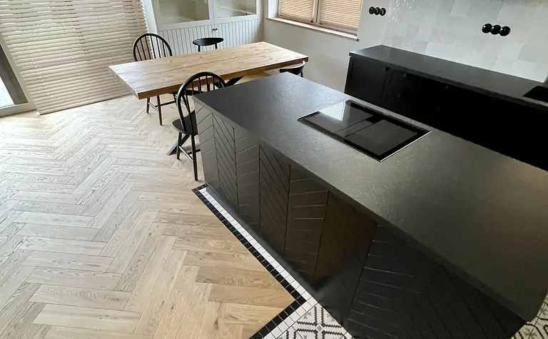 Kuchnia w stylu industrialnym z czarnymi meblami, drewnianym stołem i geometrycznym wzorem podłogi.