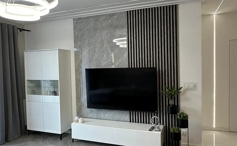 Wnętrze salonu z minimalistycznym wystrojem, nowoczesnym telewizorem i szarym dywanem.