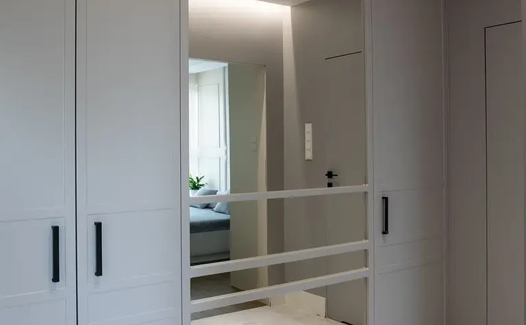 Garderoba z szarymi szafami, dużym lustrem i nowoczesnym oświetleniem. Styl art deco i tradycyjny.