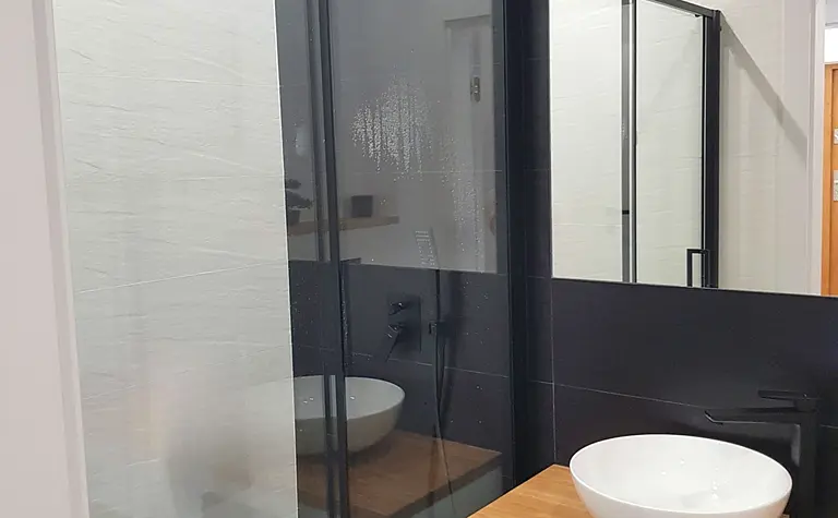 Nowoczesna łazienka z kabiną prysznicową, czarnymi akcentami i stylowymi płytkami.