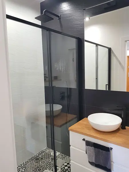 Nowoczesna łazienka z kabiną prysznicową, czarnymi akcentami i stylowymi płytkami.