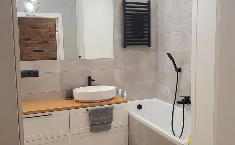 Nowoczesna łazienka z białą wanną, drewnianą umywalką, industrialnymi akcentami.