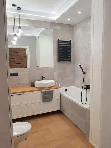 Nowoczesna łazienka z białą wanną, drewnianą umywalką, industrialnymi akcentami.