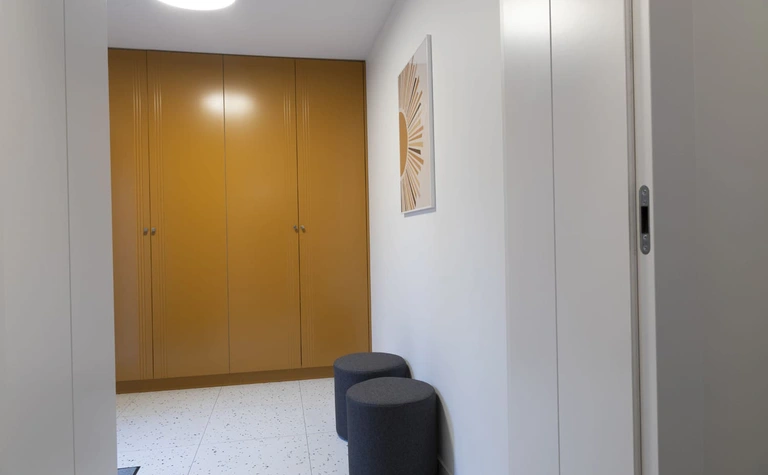 Przedpokój z szafą, szarymi siedziskami i nowoczesnym oświetleniem