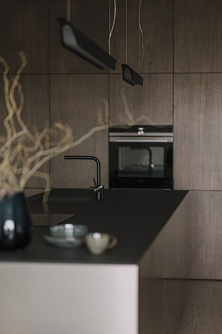 Kuchnia z ciemnymi meblami, blatem i akcesoriami w stylu minimaluxe, nowoczesnym i quiet luxury.