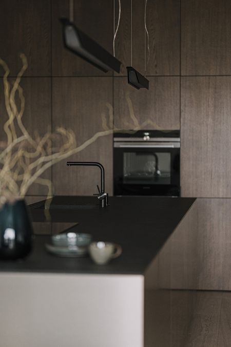 Kuchnia z ciemnymi meblami, blatem i akcesoriami w stylu minimaluxe, nowoczesnym i quiet luxury.