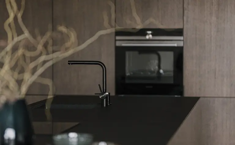 Kuchnia z ciemnymi meblami, blatem i akcesoriami w stylu minimaluxe, nowoczesnym i quiet luxury.