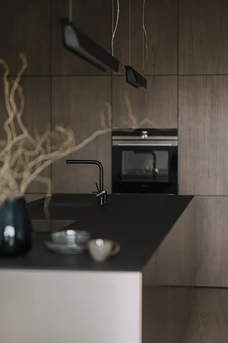 Kuchnia z ciemnymi meblami, blatem i akcesoriami w stylu minimaluxe, nowoczesnym i quiet luxury.