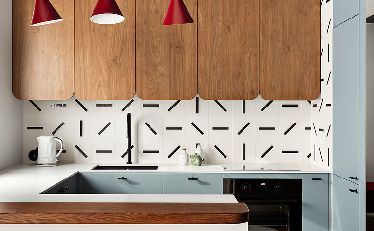 Wnętrze kuchni z drewnianymi szafkami, białym blatem i czerwonymi lampami w stylu dopamine decor.