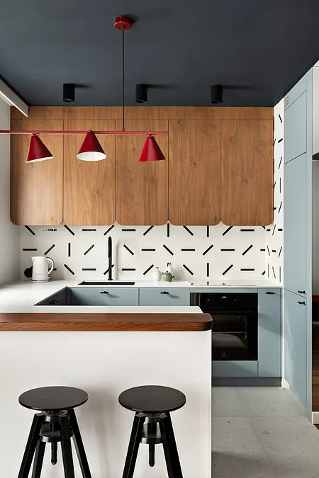 Wnętrze kuchni z drewnianymi szafkami, białym blatem i czerwonymi lampami w stylu dopamine decor.