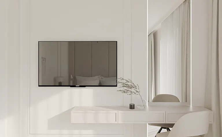 Minimalistyczne wnętrze z białym biurkiem, telewizorem i jasnymi zasłonami.