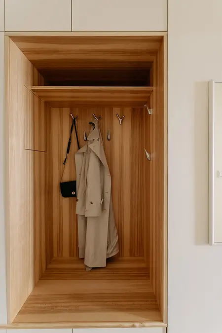 Minimalistyczna garderoba z drewnianym wnętrzem, wieszakami i płaszczem.