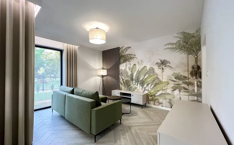 Wnętrze salonu w stylu boho i współczesnym z zieloną sofą i palmową tapetą.