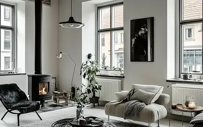 Stylowy salon w stylu skandynawskim z kominkiem, dużymi oknami, jasnymi ścianami, wygodnym fotelem, rośliną i przytulnym dywanem