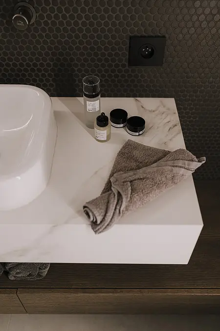 Wnętrze łazienki z białą umywalką, szarymi ręcznikami i kosmetykami. Styl minimaluxe, nowoczesny, quiet luxury, współczesny.