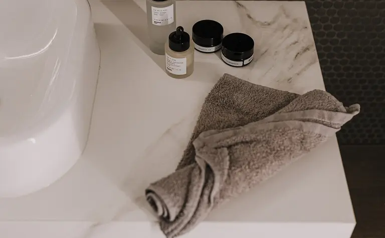 Wnętrze łazienki z białą umywalką, szarymi ręcznikami i kosmetykami. Styl minimaluxe, nowoczesny, quiet luxury, współczesny.