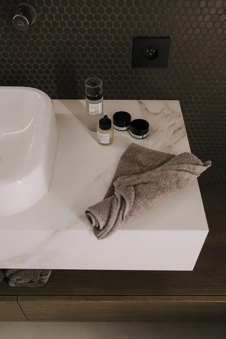 Wnętrze łazienki z białą umywalką, szarymi ręcznikami i kosmetykami. Styl minimaluxe, nowoczesny, quiet luxury, współczesny.