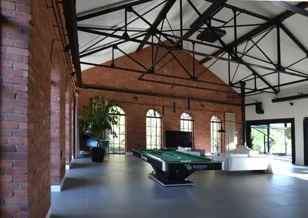 Wnętrze w stylu industrialnym z zielonym stołem do bilarda i wysokimi oknami.
