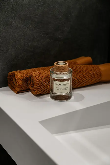 Wnętrze łazienki z brązowymi ręcznikami i dyfuzorem zapachowym na białej umywalce.