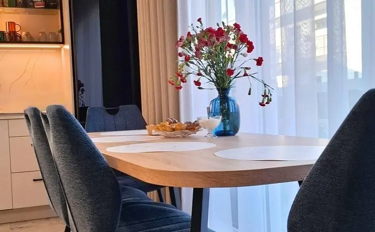 Wnętrze jadalni z drewnianym stołem, niebieskimi krzesłami i kwiatami w wazonie.