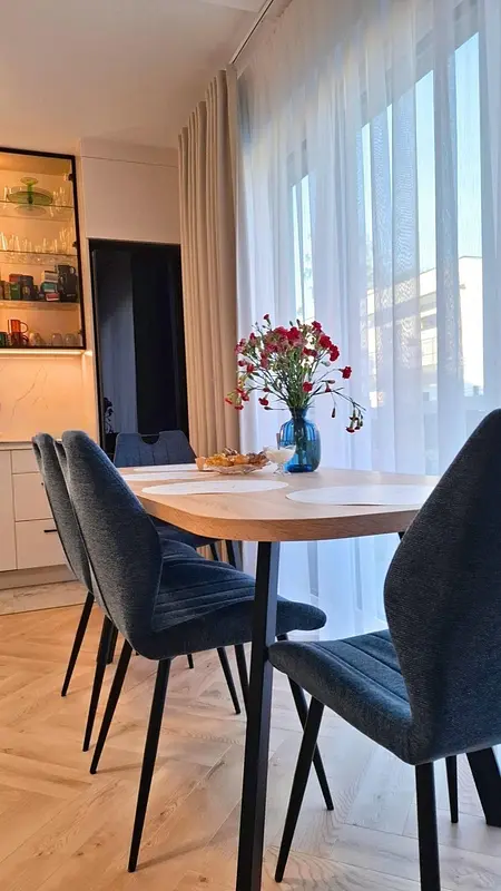 Wnętrze jadalni z drewnianym stołem, niebieskimi krzesłami i kwiatami w wazonie.