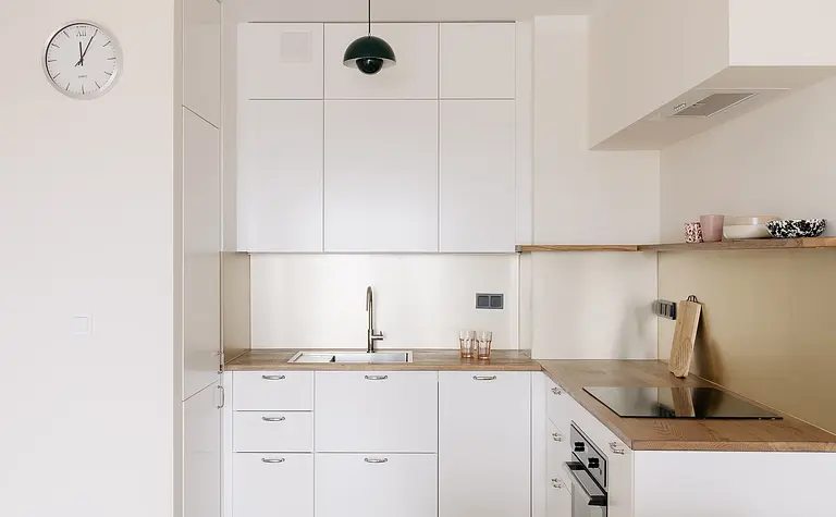Kuchnia w stylu minimalistycznym z białymi meblami i drewnianym akcentem.