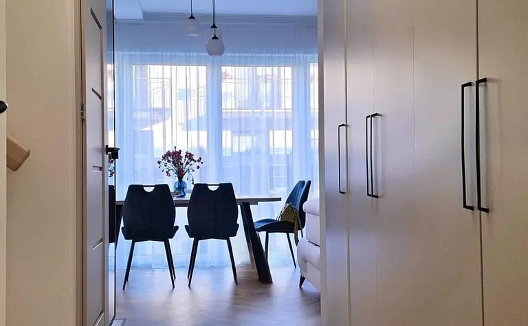 Przedpokój z białymi meblami, drewnianą podłogą i nowoczesnymi lampami.