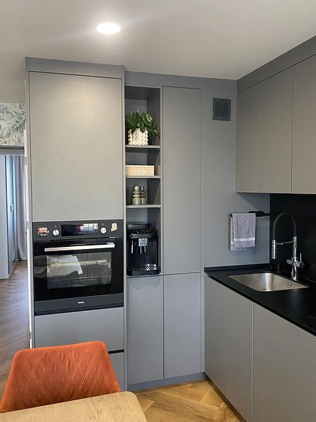 Nowoczesna kuchnia z szarymi meblami i czarnym blatem, minimalistyczny styl.