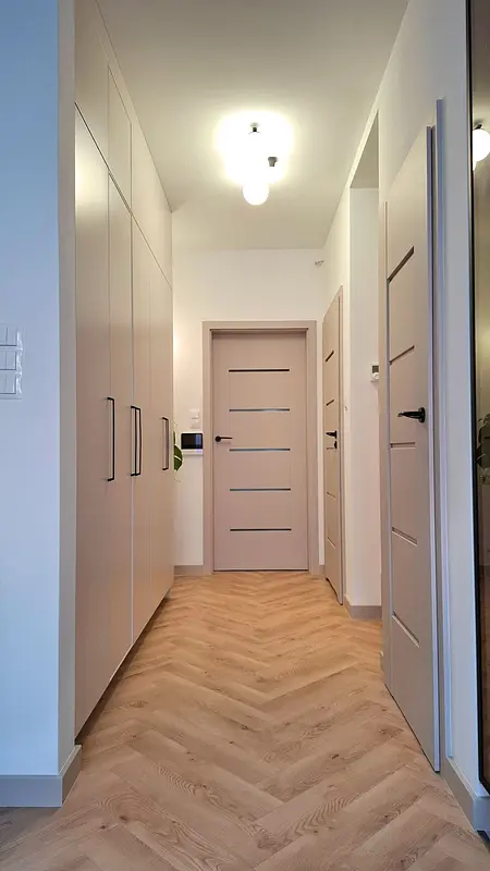 Stylowy przedpokój z jasnymi szafkami i podłogą w jodełkę, nowoczesny i skandynawski.